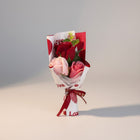 eRamis bouquet of artificial red and pink roses with green leaves, wrapped in white paper with red hearts and "Love" text.
