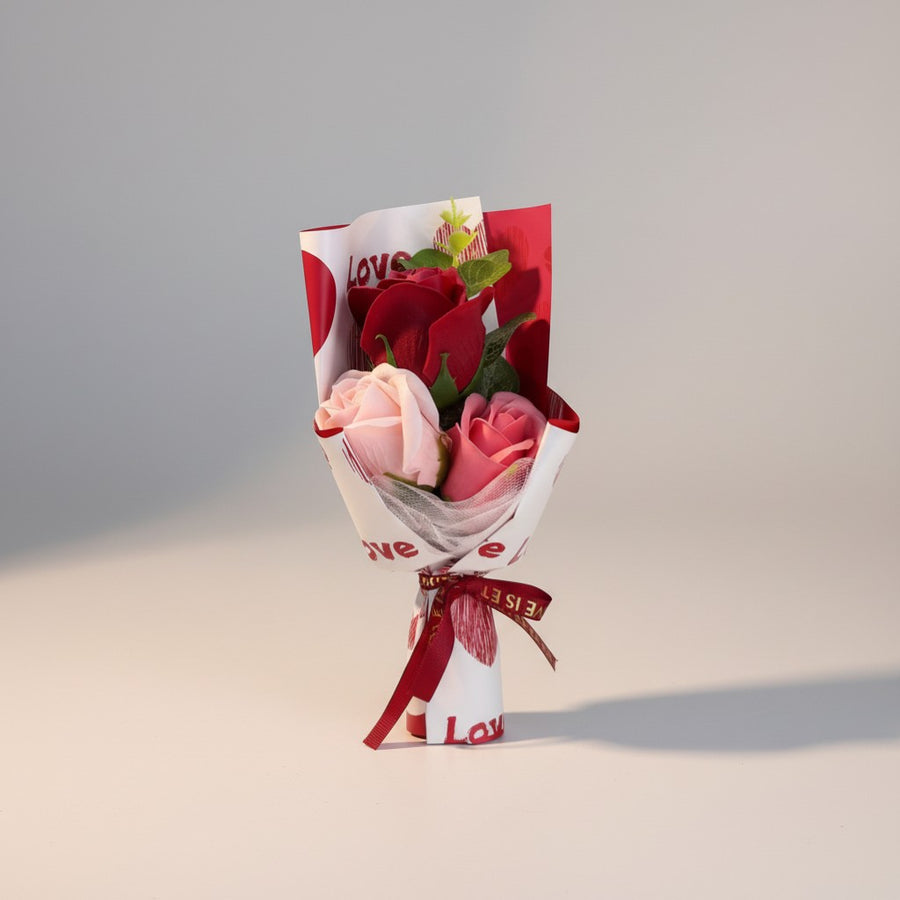 eRamis bouquet of artificial red and pink roses with green leaves, wrapped in white paper with red hearts and "Love" text.