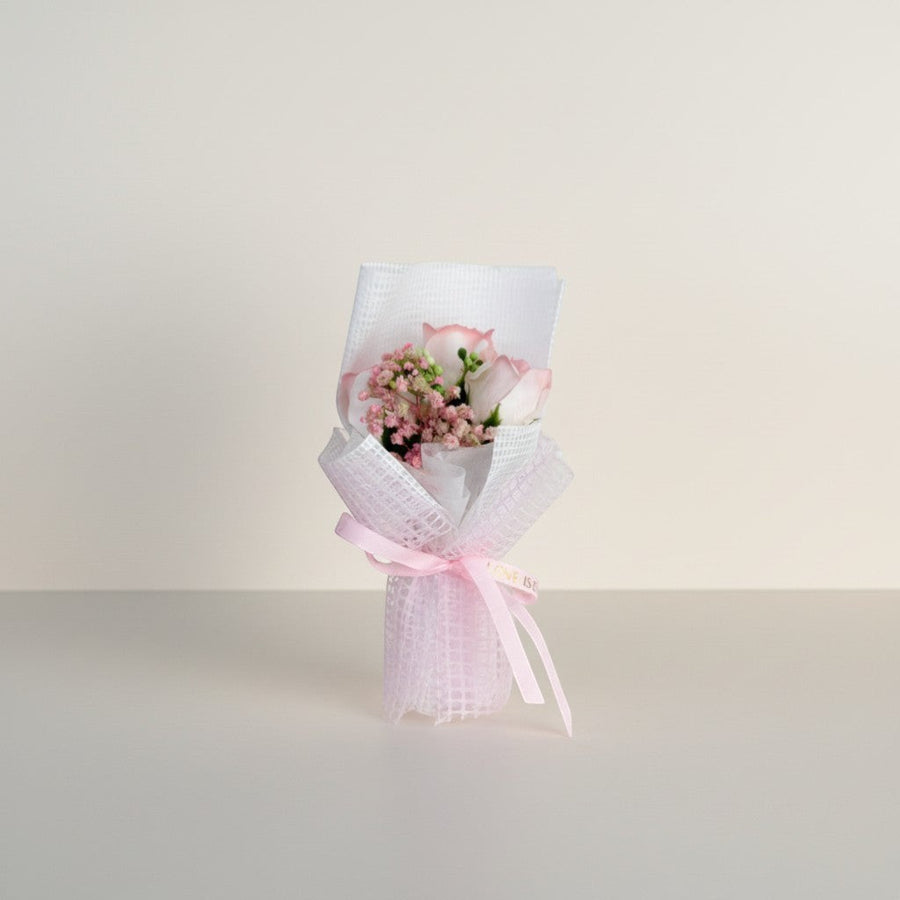 eRamis pink roses and baby's breath bouquet wrapped in white mesh and tied with a pink ribbon.