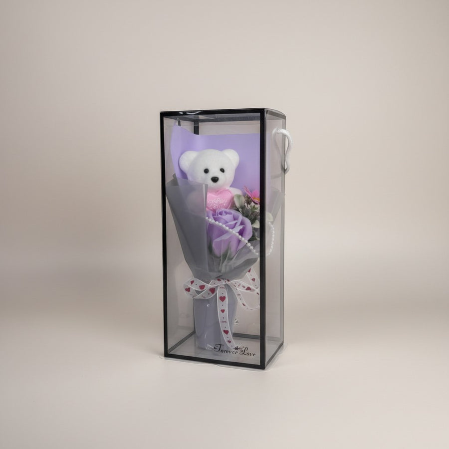 eRamis white plush teddy bear with pink heart saying "I Love You", next to a purple soap rose, in a clear box with ribbon.