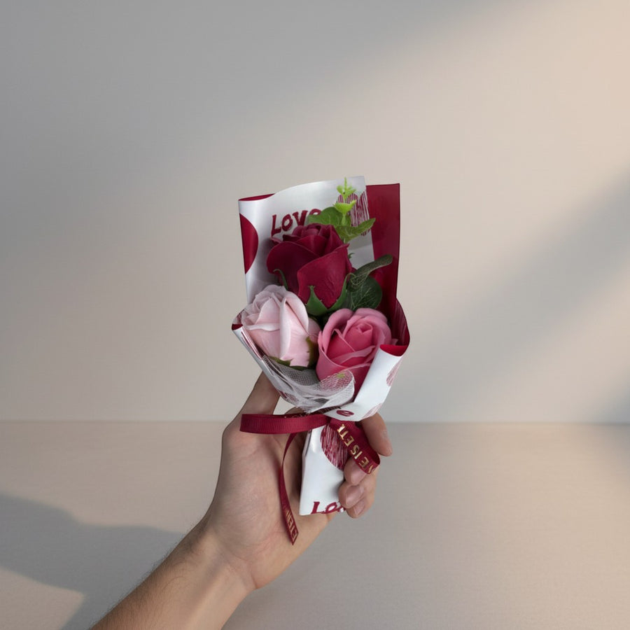 eRamis bouquet of red and pink soap roses with green leaves, wrapped in white paper with red hearts and 'Love' text, tied with a red ribbon.