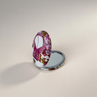 eRamis round compact mirror with a pink ribbon and floral design. Features a silver metal casing.