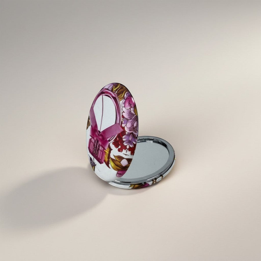 eRamis round compact mirror with a pink ribbon and floral design. Features a silver metal casing.