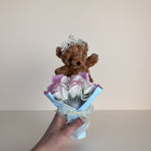 eRamis brown teddy bear wearing a tiara holding a bouquet of pink and white roses with pearl accents.