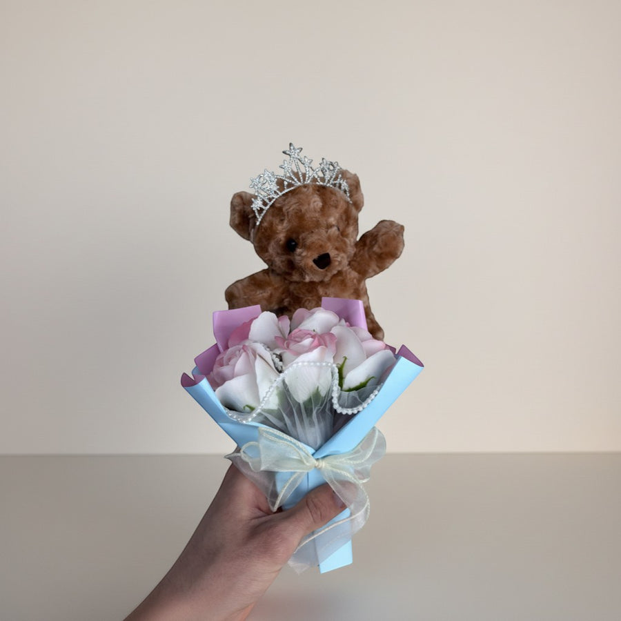 eRamis brown teddy bear wearing a tiara holding a bouquet of pink and white roses with pearl accents.