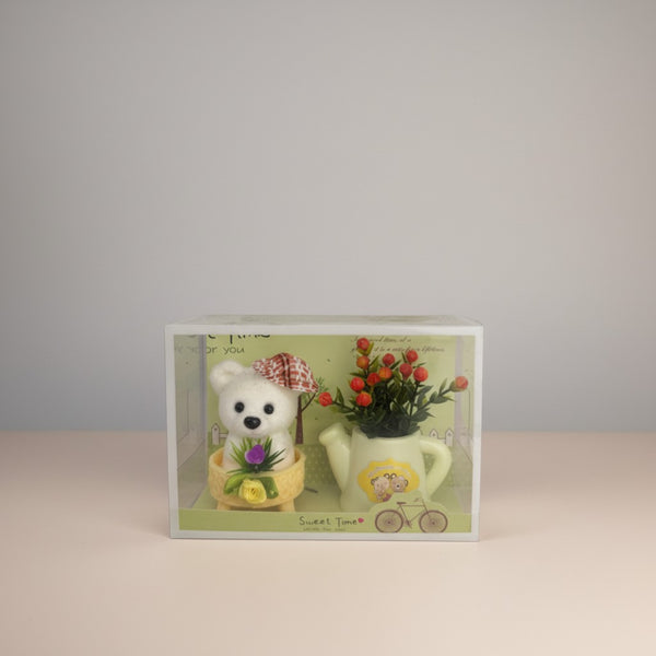 eRamis white teddy bear with red plaid hat and green floral decor in a yellow basket next to a watering can with flowers.