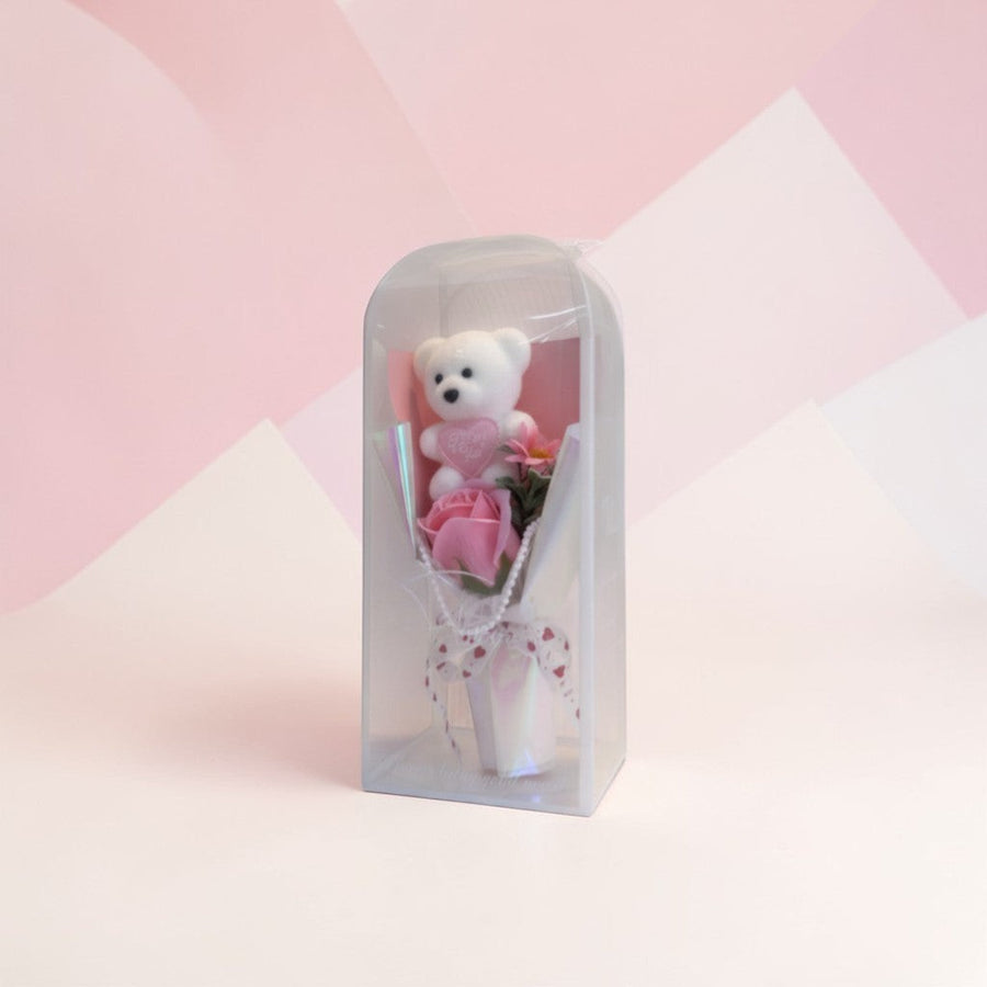 eRamis white teddy bear with pink heart saying I Love You, surrounded by pink roses and flowers, in a clear display box.