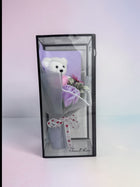 eRamisHere white teddy bear with purple rose bouquet in clear box, tied with heart ribbon.