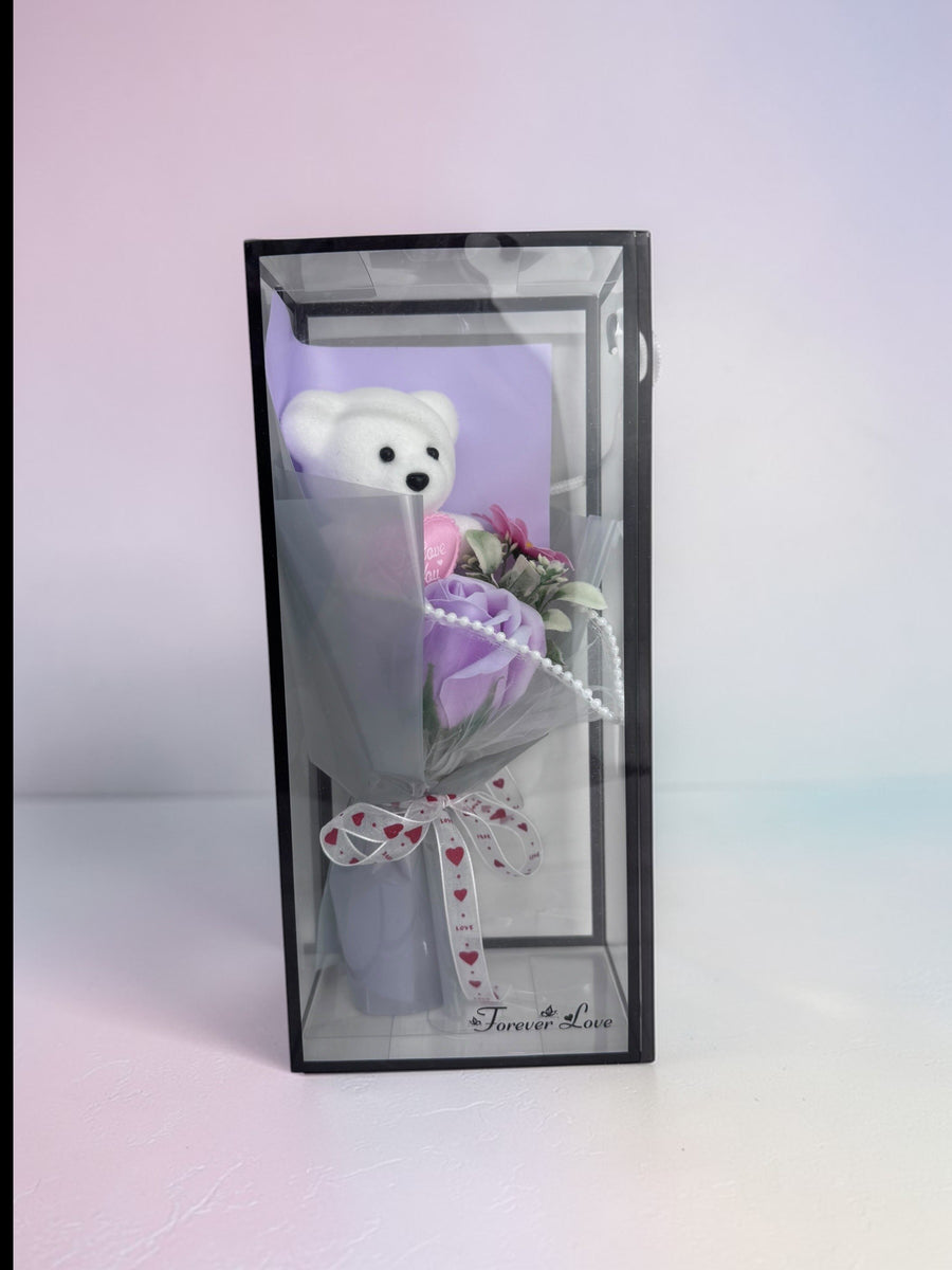 eRamisHere white teddy bear with purple rose bouquet in clear box, tied with heart ribbon.