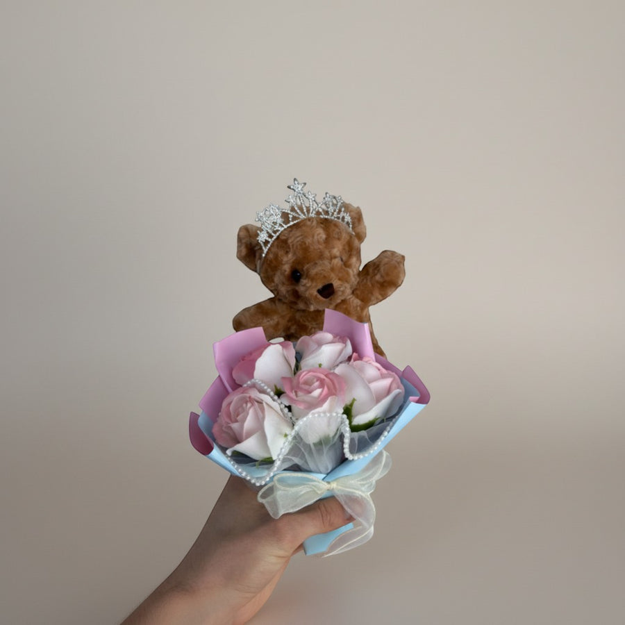 eRamisHere brown teddy bear wearing a tiara holding a bouquet of pink and white roses with pearls.