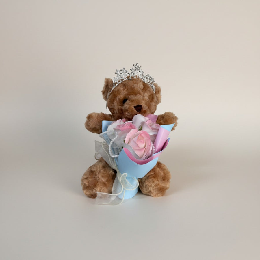 eRamisHere brown teddy bear wearing a tiara, holding a bouquet of pink and white roses with pearl accents.