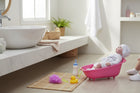 eRamis baby doll in pink polka dot robe and hat sits in a pink bathtub with accessories including a rubber ducky and bottle.