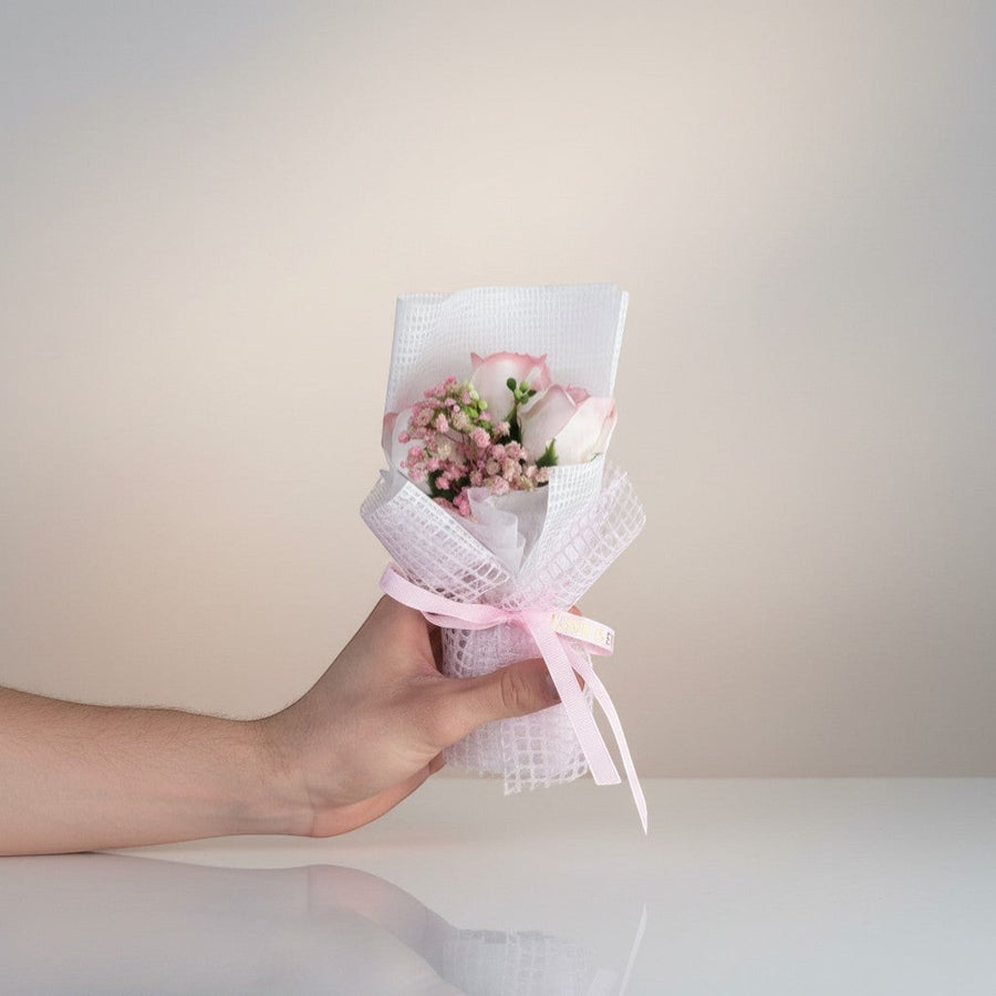 eRamis pink roses and baby's breath bouquet, wrapped in white mesh with a pink ribbon that says "LOVE IS E".